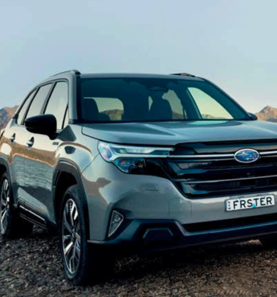 Front view of the 2026 Subaru Forester Hybrid parked by a lake with mountain scenery in the background.