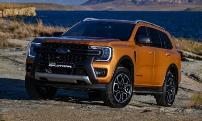 Ford Everest Wildtrak in Luxe Yellow parked on rocky terrain near a lake with mountains in the background.