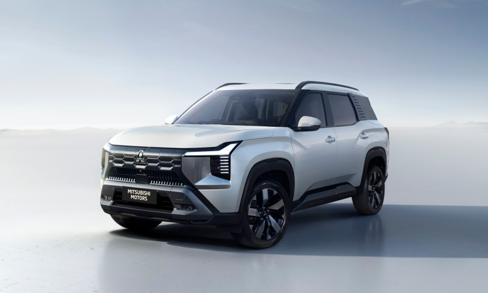 Front three-quarter view of the Mitsubishi Destinator SUV in silver, showcasing its bold Dynamic Shield grille, T-shaped LED headlights, and sculpted body under a clear sky.