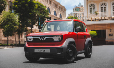 A red VinFast VF 3 electric micro-SUV parked on a city street under bright sunlight.