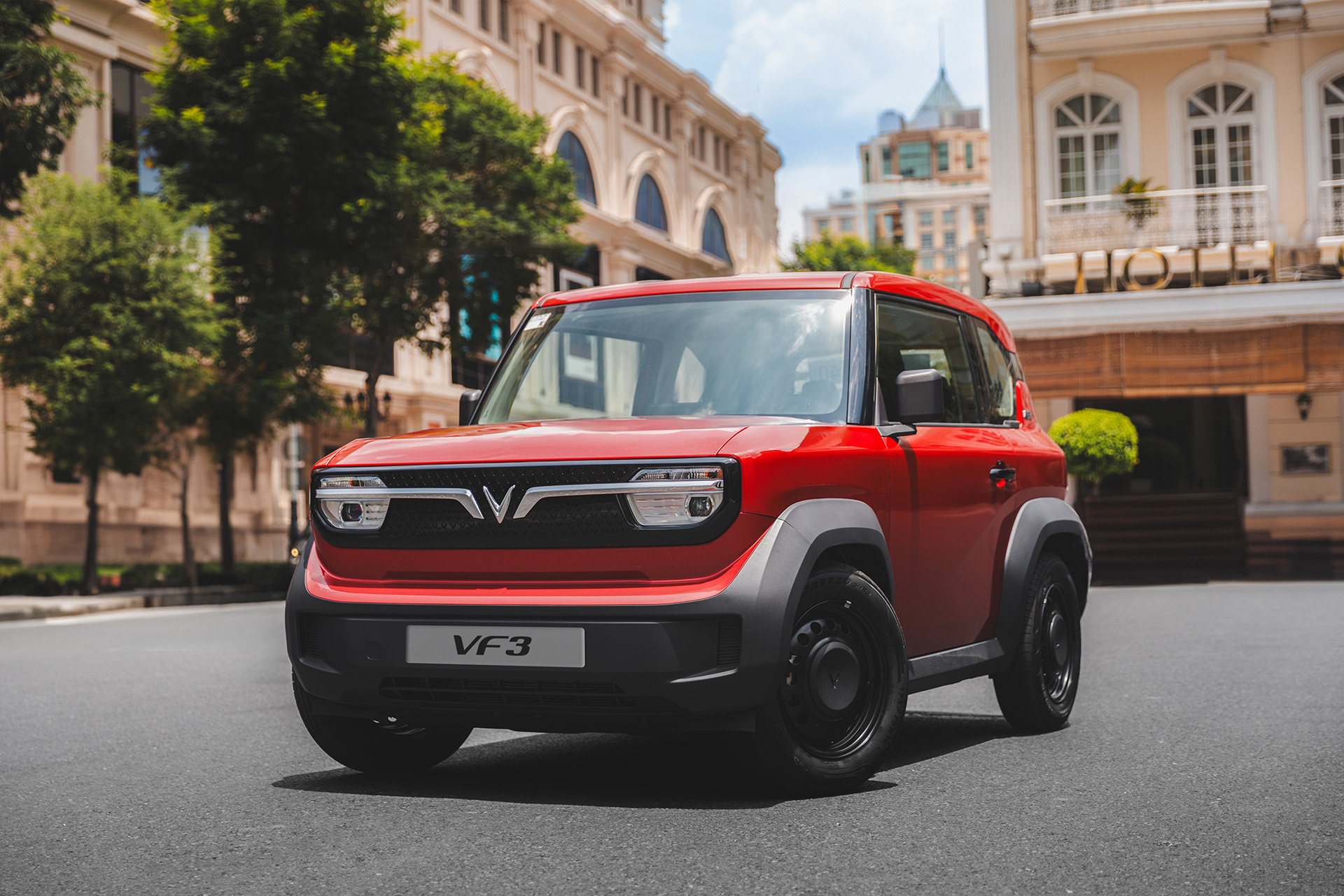 A red VinFast VF 3 electric micro-SUV parked on a city street under bright sunlight.