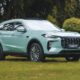 A mint-green Jetour X70 i-DM SUV parked on a grassy area, highlighting its bold front grille and sleek LED lighting design.