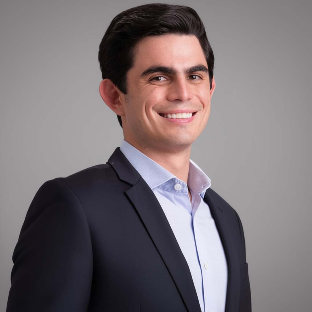 A man in a dark suit and light blue shirt smiles confidently against a neutral background.