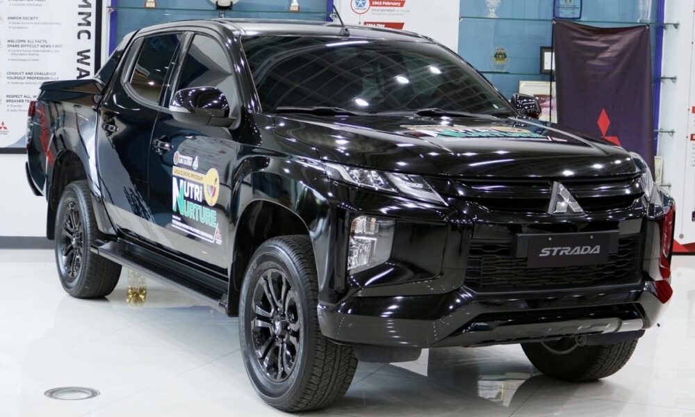 A black Mitsubishi Strada Athlete pickup on display at the MMPC showroom, bearing the UPLB DUNONG Nutri-Nurture Project logo on its doors.