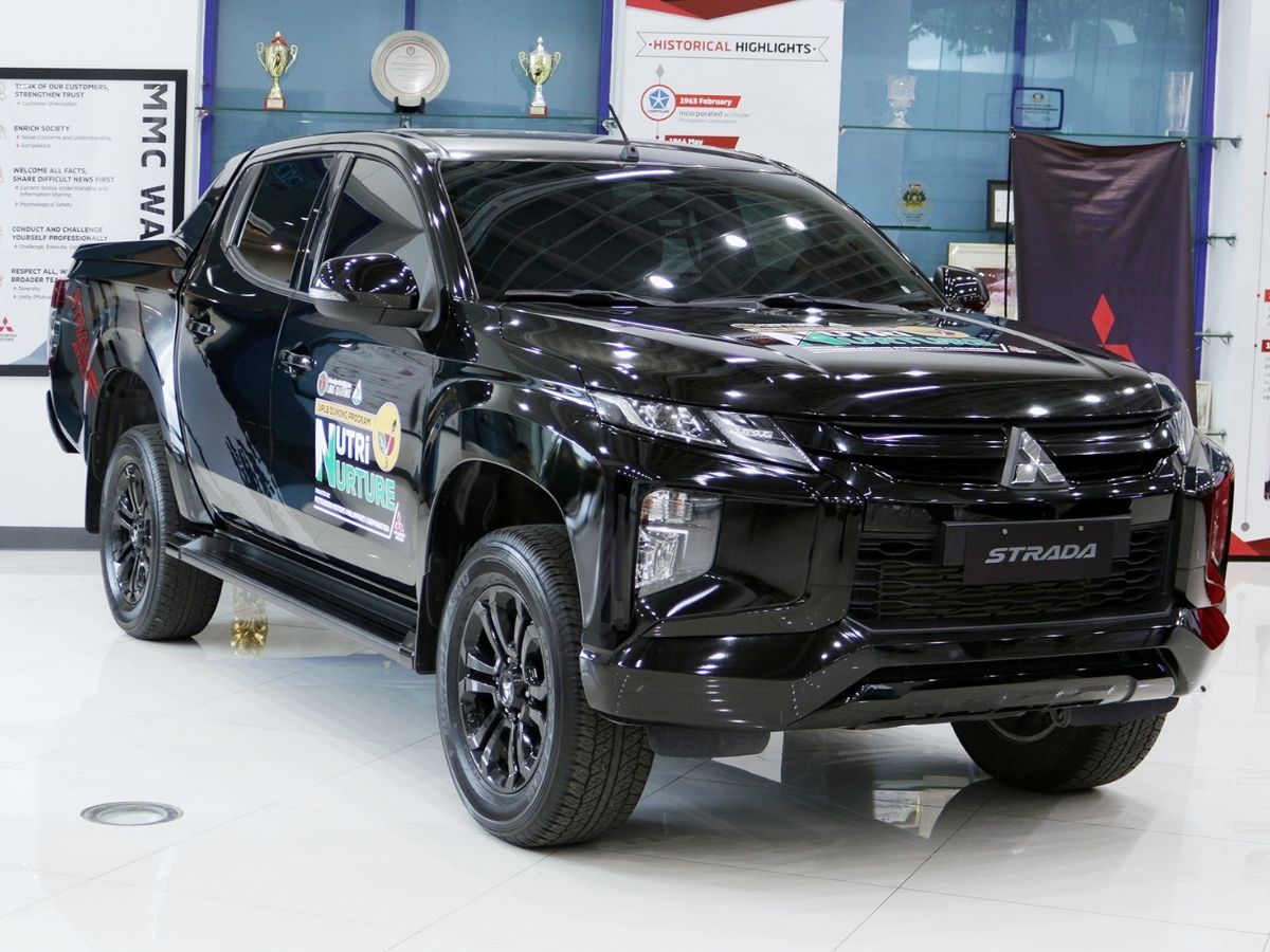 A black Mitsubishi Strada Athlete pickup on display at the MMPC showroom, bearing the UPLB DUNONG Nutri-Nurture Project logo on its doors.